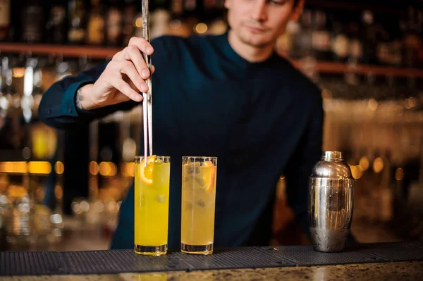 Unga bartender förbereder två alkoholhaltiga drinkar, att lägga bitar av orange — Stockfoto