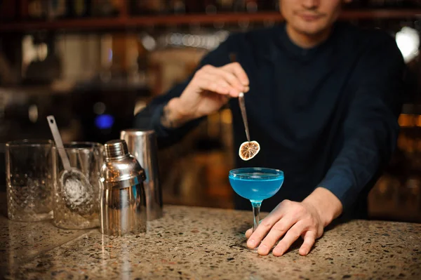Barman kompletterar den blå lagunen alkohol cocktailen med en skiva av torkade citrus — Stockfoto