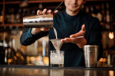 Bir shaker yağan taze içki barmen süzgeç kullanarak bir cam içine gülümsüyor