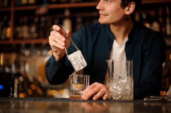 Guapo camarero poniendo un gran cubo de hielo en un vaso — Foto de Stock