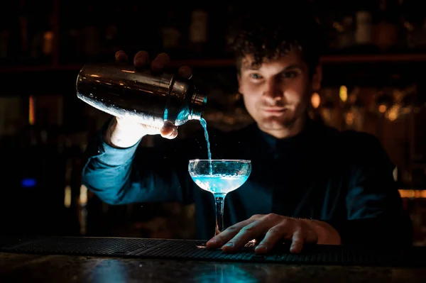 Unga leende bartendern hälla fräsch drink med blå sprit från en shaker i ett glas med hjälp av SIL — Stockfoto