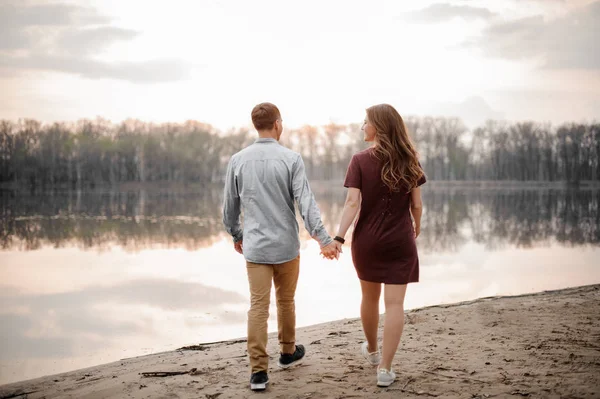 Casal apaixonado andando em uma areia molhada ao longo do lago no fundo das árvores — Fotografia de Stock
