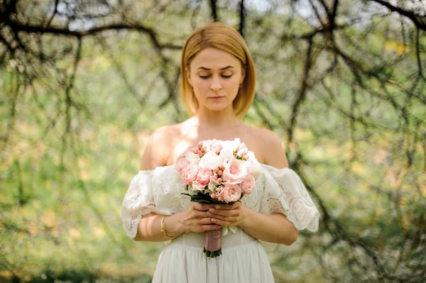 Chica de pie entre ramas de árbol blanco con un ramo de color rosa — Foto de Stock