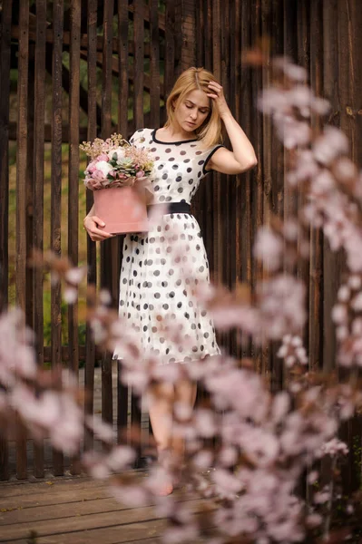 Chica joven de pie cerca de la valla con una caja de flores — Foto de Stock