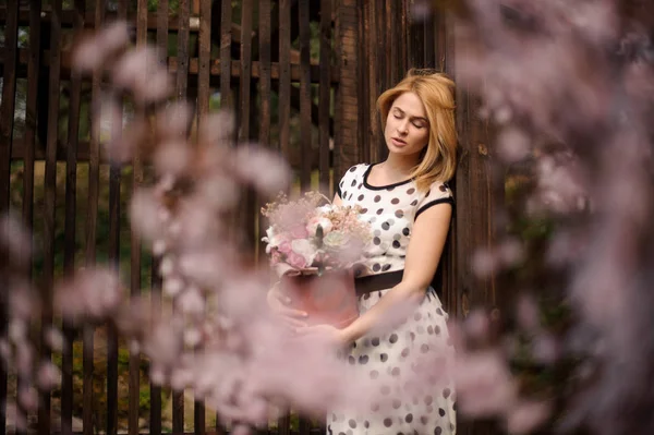 Menina de pé perto da cerca com uma caixa rosa de flores — Fotografia de Stock