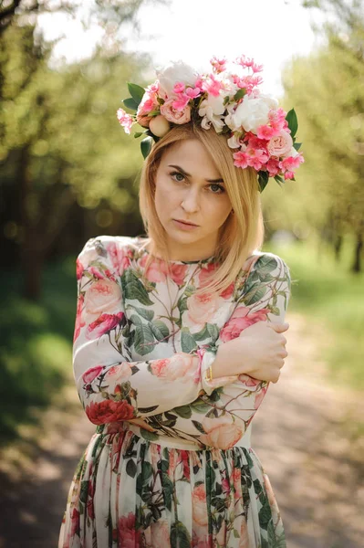 Chica joven en una diadema de flores de pie entre los árboles — Foto de Stock