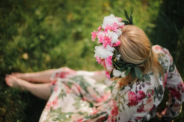 Ung och vacker flicka i en blomma diadem sitter på gräset — Stockfoto