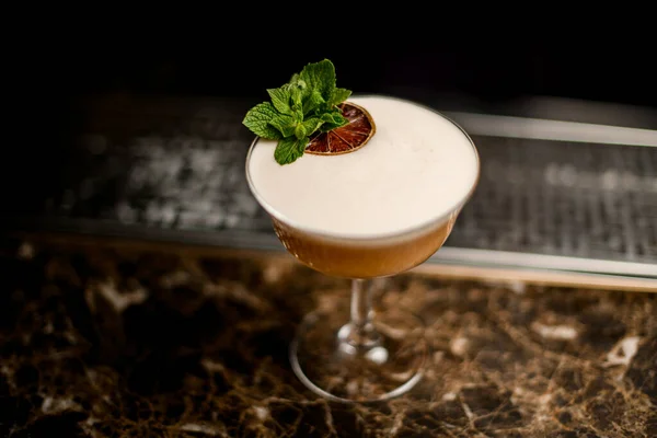 Cocktail alcolico nel bicchiere decorato con un ramo di foglia di menta e una fetta di arancia essiccata — Foto Stock