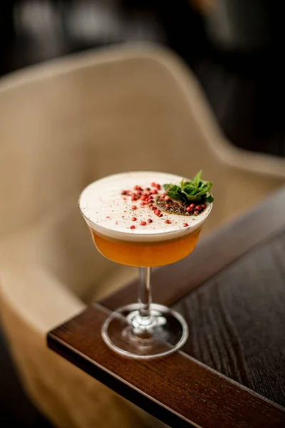Delizioso cocktail alcolico nel bicchiere decorato con foglia di menta, grani di pepe e fetta di arancia secca sul tavolo. — Foto Stock