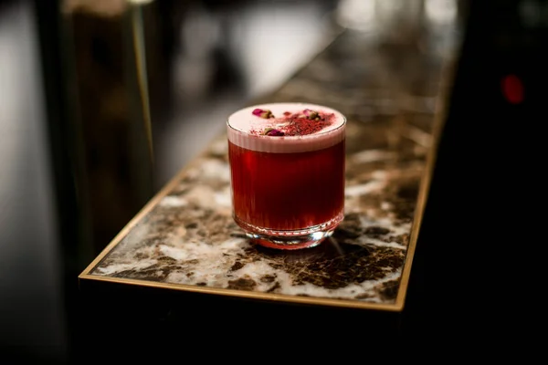Cocktail alcolico rubino con schiuma nel bicchiere decorato con spezie e boccioli di rosa poco essiccati — Foto Stock