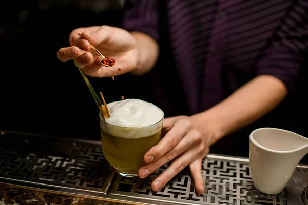 Bartender adding to the cocktail decorating with a whipped cream with a tropical leaf and dried orange a red pepper peas