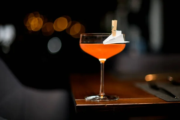 Oranje alcoholische cocktail in het glas versierd met een papieren vliegtuigje in de wasknijper — Stockfoto