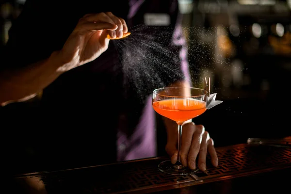 Cantinero pulverización en el cóctel en el vaso decorado con avión de papel con pinza de ropa con un jugo de ralladura de naranja — Foto de Stock