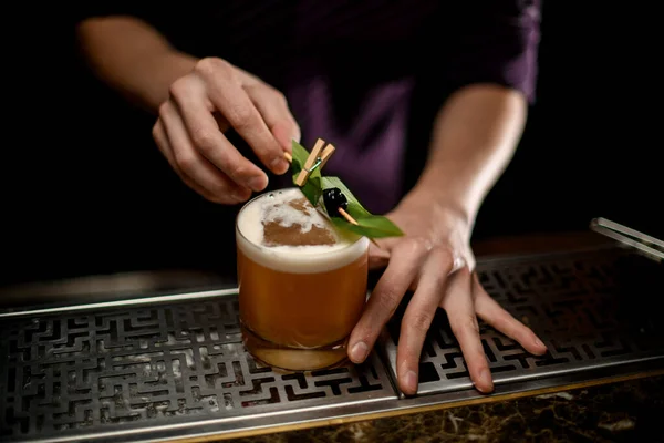 Man bartender dekorerade ett glas med krämig färg cocktail dryck med en grön tropisk blad och svart bär på tandpetaren — Stockfoto