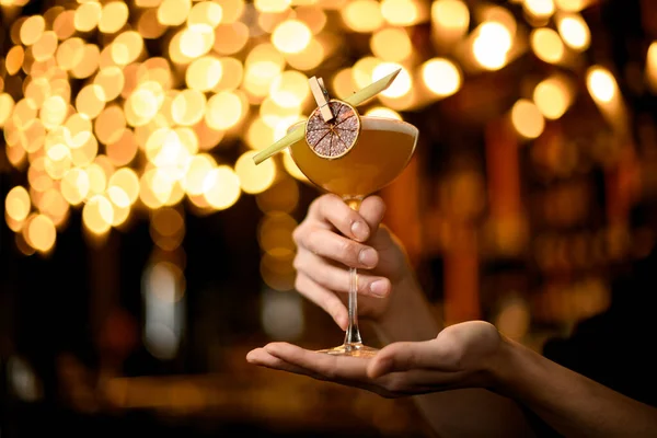 Barista maschile che serve cocktail alcolici gialli nel bicchiere con limone e foglia secchi — Foto Stock