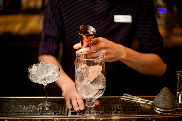 Barista maschile che versa una bevanda alcolica dal jigger a un bicchiere da cocktail con cubetti di ghiaccio — Foto Stock