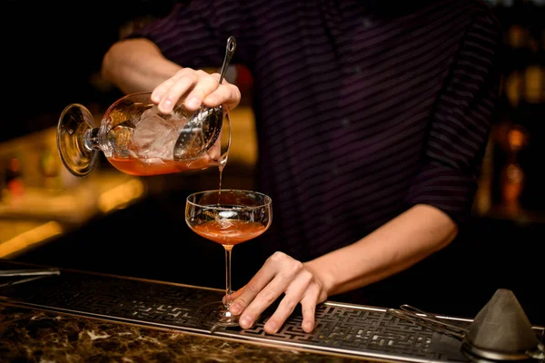 Barman profissional derramando uma bebida alcoólica do um copo com cubo de gelo para outro vazio — Fotografia de Stock