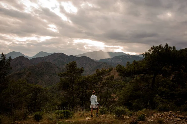Fille avec les bâtons de marche debout sur le rocher regardant les montagnes à travers les arbres — Photo