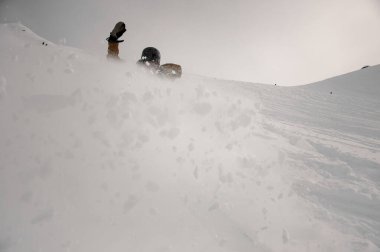 Profesyonel felçli snowboardcu karla kaplı tepeden aşağıya doğru beyaz bir sıçrama yapıyor.