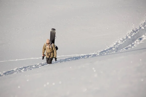 L'uomo che cammina sul sentiero calpestato dalla neve con lo snowboard alle spalle — Foto Stock