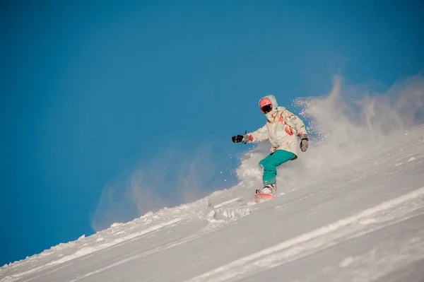 Nő snowboardos lovaglás le a hegyről a háttérben a tiszta ég — Stock Fotó