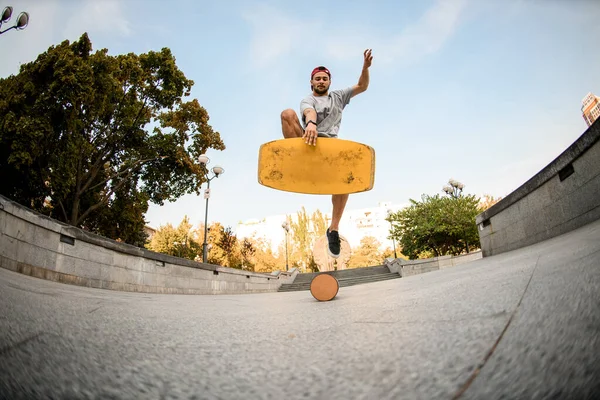 Fish-eye shot from below man jumping on the yellow balance board on the concrete border — Stock Photo, Image