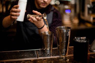Erkek barmen alkollü bir içeceği jiggerdan çeliğe dolduruyor.