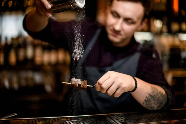 Mężczyzna barman dodając cukier w proszku dla w brownie kawałki na szpikulec — Zdjęcie stockowe