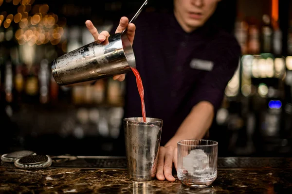 Männlicher Barkeeper, der einen roten Cocktail von der einen Hälfte des Stahlshakers zur anderen gießt — Stockfoto