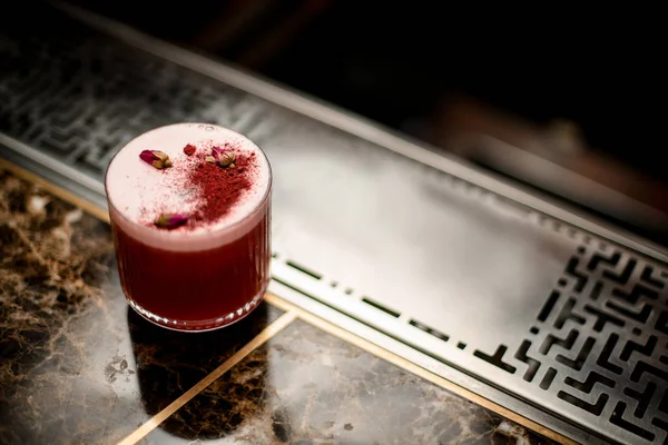 Cóctel alcohólico rojo con una escoria en el vaso decorado con especias y pequeños capullos de rosa secos — Foto de Stock