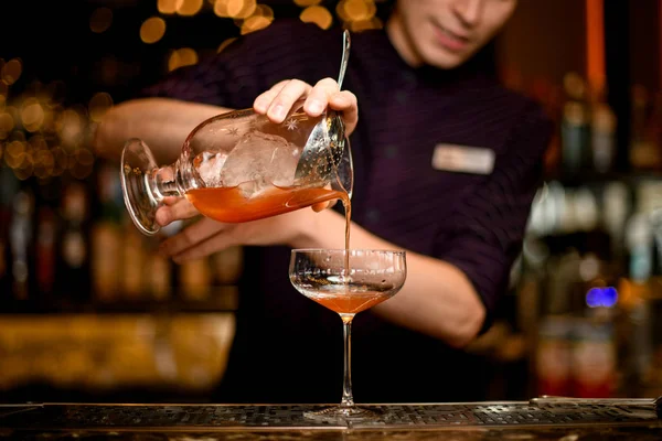 Männlicher Barkeeper, der ein alkoholisches Getränk aus dem einen Glas mit Eiswürfel ins andere leert — Stockfoto