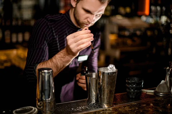 Barman adicionando uma essência marrom da pipeta a uma bebida alcoólica em uma coqueteleira de aço — Fotografia de Stock