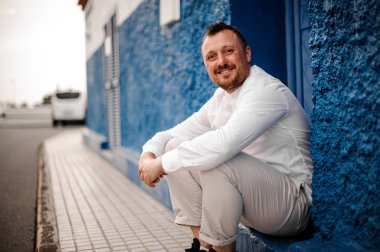 Beyaz elbiseli bir adam eşikte oturuyor.