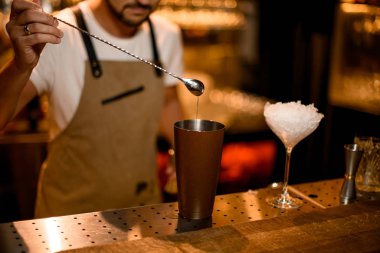 Barmen uzun çubuk kaşıkla kokteyl doldurur.