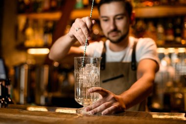 Barmen uzun çubuk kaşıkla kokteyl dolduruyor.