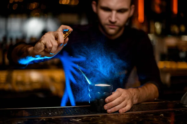 Mężczyzna barman tarło na czarny szklanka z pyszny koktajl z istota w niebieski światło — Zdjęcie stockowe
