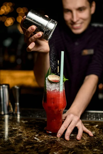 Professioneller Barkeeper bestreut das mit Eis, Limette und tropischem Blatt verzierte Cocktailglas mit einem Zuckerpulver — Stockfoto