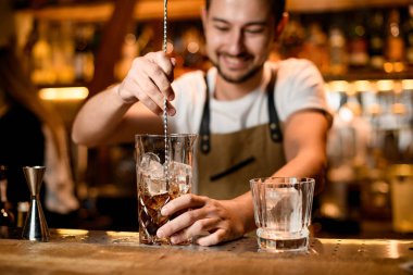 Bartender stirring alcohol with ice in glass
