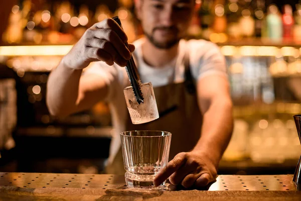 Bartender puts ice in glass with forceps