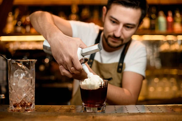 Bartender adds whipped cream to alcohol cocktail — стокове фото