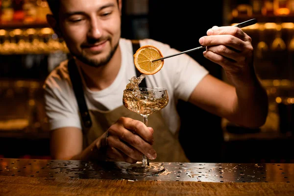Un barman souriant met une tranche d'orange dans une boisson alcoolisée — Photo