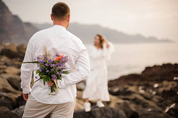 Mužský ženich v bílé košili s kyticí vzadu stojící na pobřeží a dívající se na nevěstu — Stock fotografie