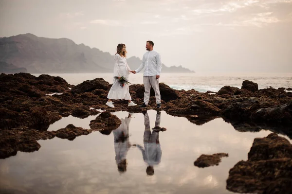 Muž ženich a žena nevěsta kráčející po skalnaté pláži — Stock fotografie