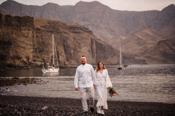 Muž ženich a žena nevěsta kráčející po skalnaté pláži — Stock fotografie