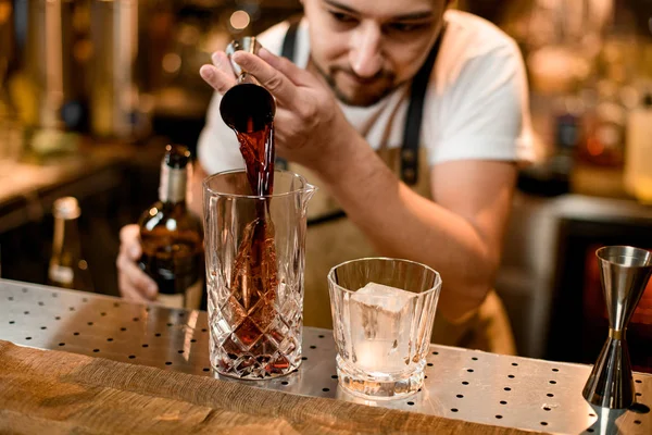 Cantinero vertiendo una bebida alcohólica marrón del jigger a un vaso de mezcla — Foto de Stock