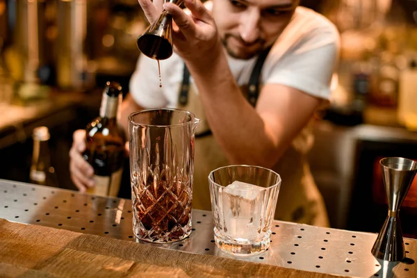 Cantinero profesional que vierte una bebida alcohólica marrón del jigger a un vaso de mezcla — Foto de Stock