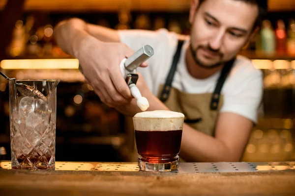 Чоловік бармен додає збитих вершків до коричневого коктейлю в склянці — стокове фото