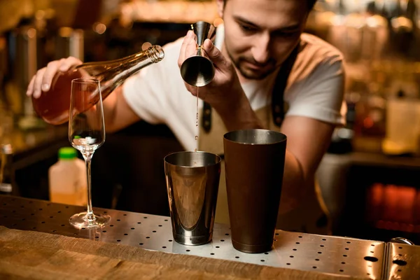 Barman masculino derramando uma bebida alcoólica laranja do jigger para uma coqueteleira de aço marrom — Fotografia de Stock