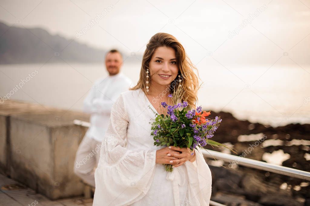 Female bride in white dress standing on the seaside with her groom