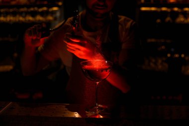 Profesyonel barmen bardağa kırmızı ışıkta acı püskürterek kokteyl sıkıyor.